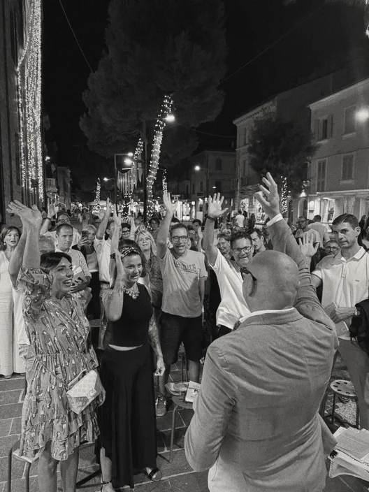 Gabriele Micozzi di spalle, le mani alzate con la folla durante una festa di strada