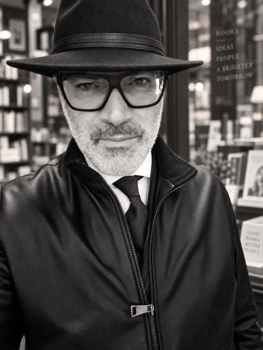 Gabriele Micozzi con cappello e occhiali davanti alla vetrina di una libreria, ritratto in bianco e nero